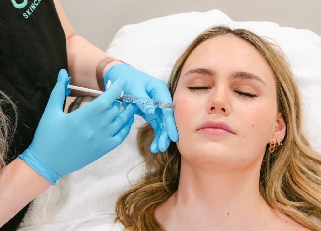 A woman lying on a treatment bed while gloved hands inject her cheek with Botox Near Brentwood, TN.